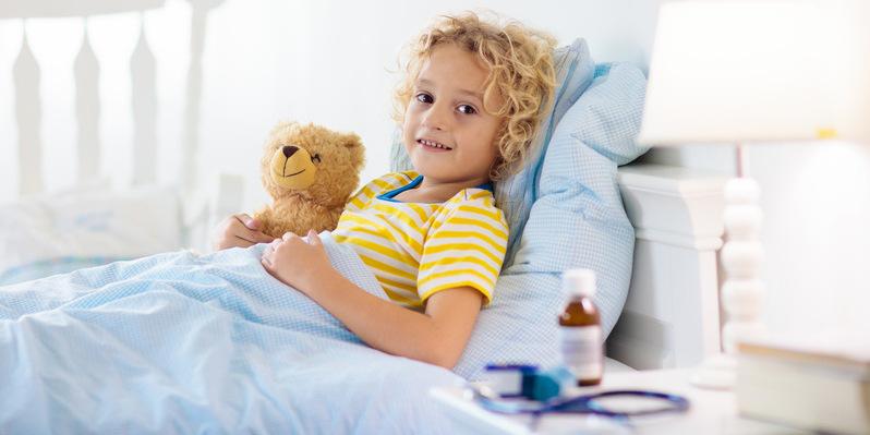 Kiedy zbijać gorączkę? Od jakiej temperatury? Dziecko leży w łóżku i trzyma ulubionego pluszowego misia.